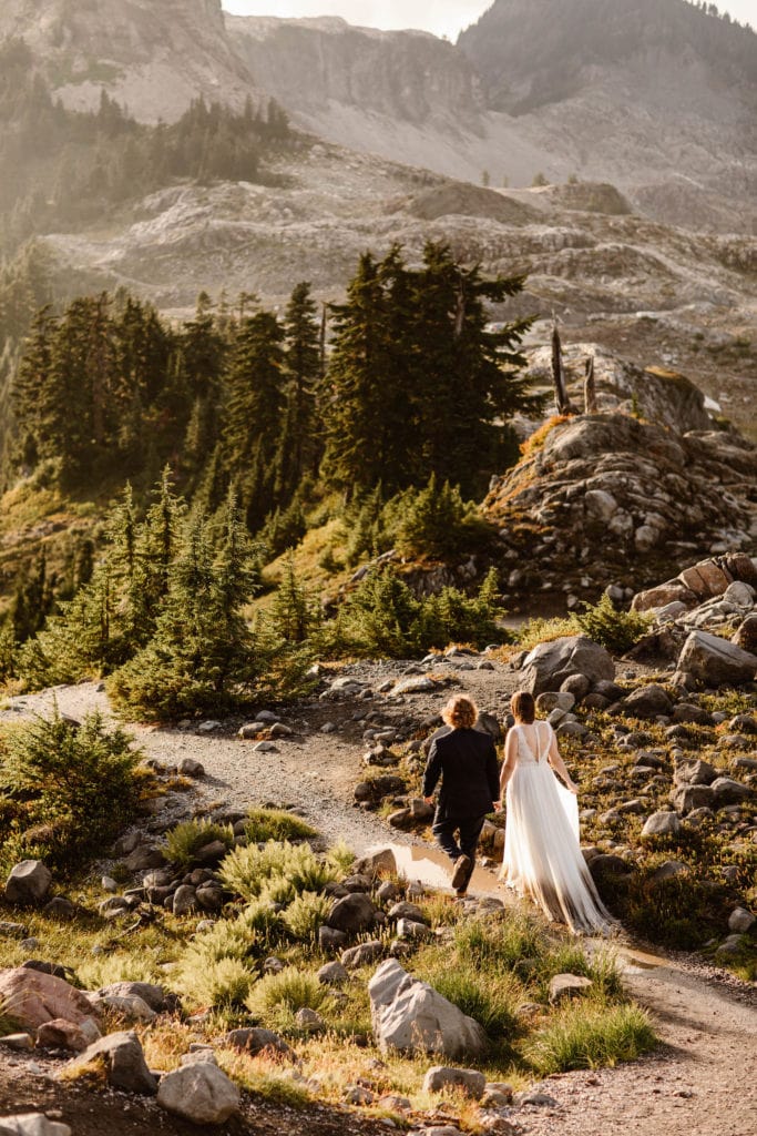couple making their way down a trail in flowy summer elopement dresses