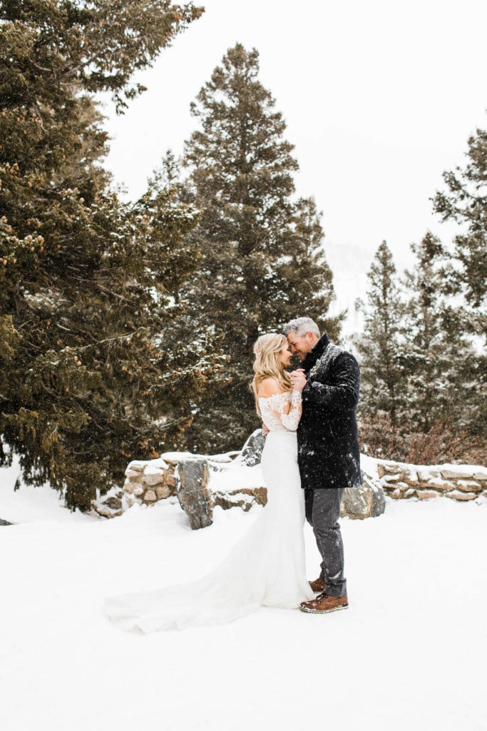 couple sharing their first dance in the snow while the bride wears a lace off shoulder elopement dress for winter