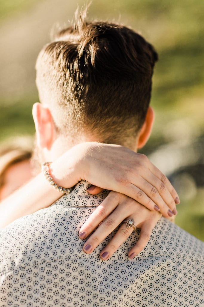 woman displaying her engagement ring with her hands around her fiance's neck after he proposes marriage