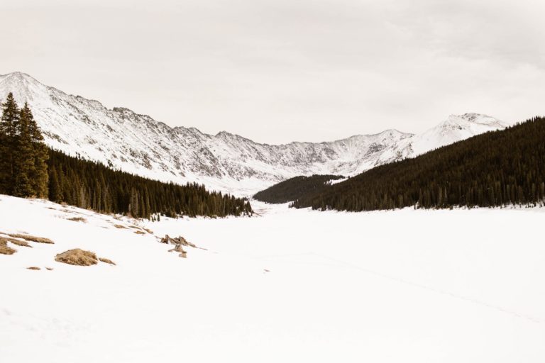 wide angle view of the reservoir covered in snow with trees in front of the mountains