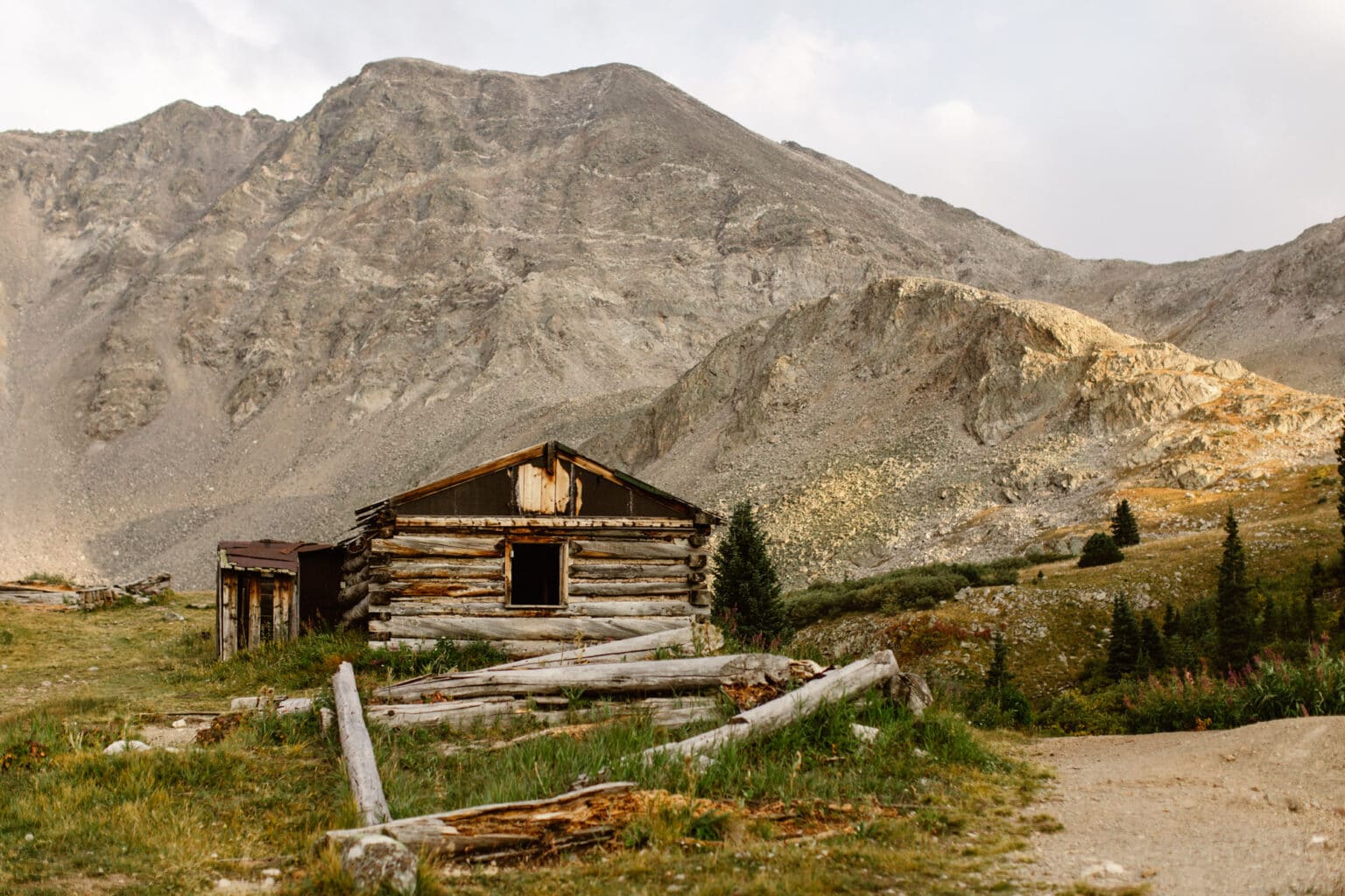 abandoned 1800s cabin with mountains towering above it on Mayflower Gulch Trail in Colorado in the summer