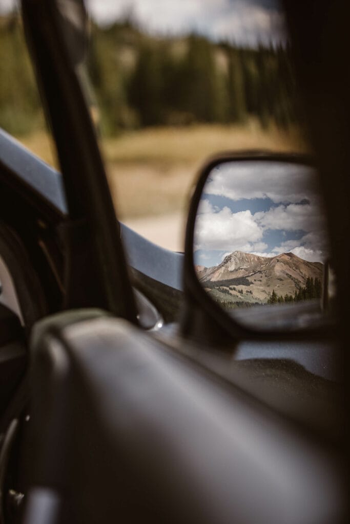 view of the mountains on a sunny day in Crested Butte as seen through the side mirror of a black car