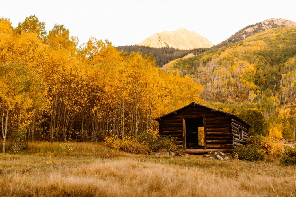 log cabin situated near the parking lot at Ashcroft Ghost Town Colorado surrounded by yellow aspen trees and a mountain peak bathing in orange alpenglow
