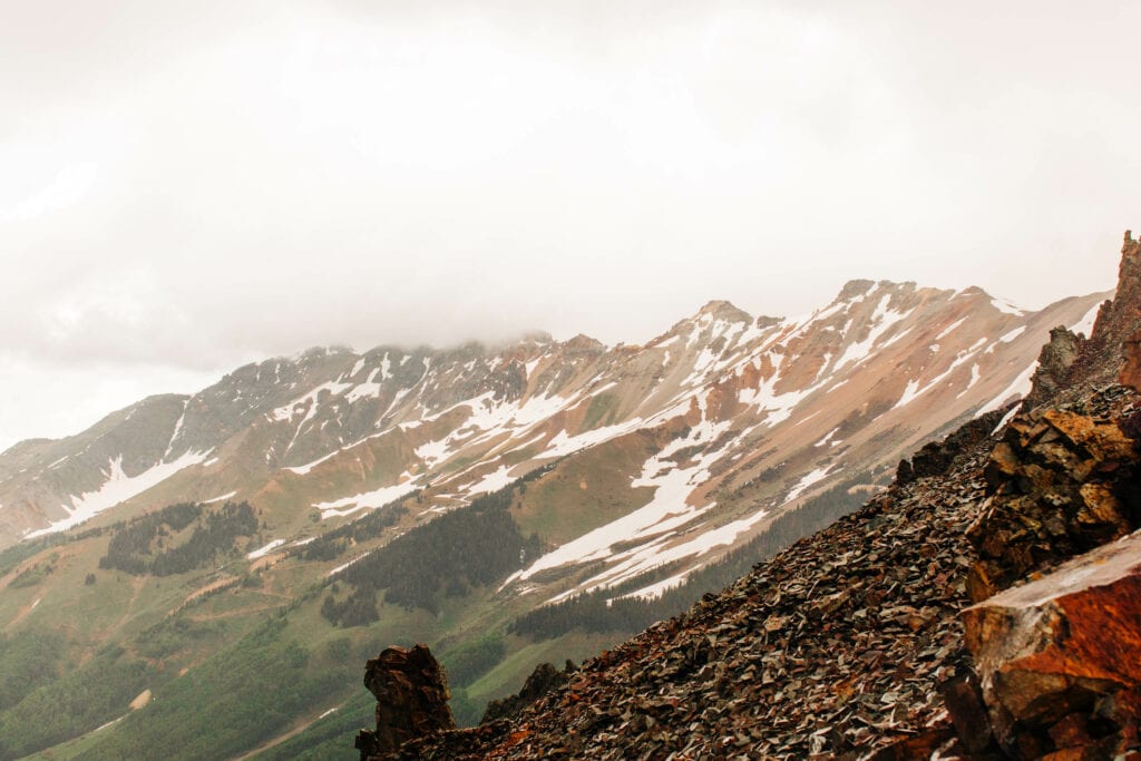 red hued mountains on Ophir Pass in Colorado with snow dotting them on a moody cloudy day