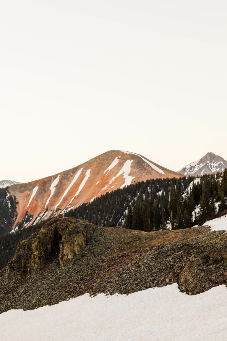 red hued mountain along Ophir Pass in Colorado with a snowfield sitting in front of it
