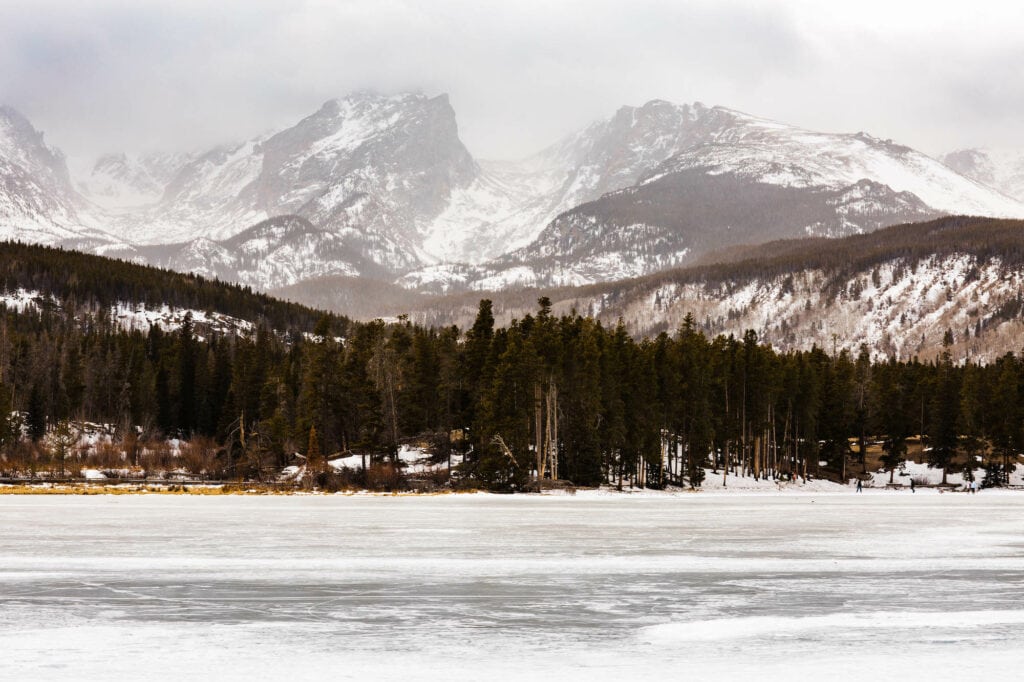 snow covered Colorado mountains towering over the frozen Sprague Lake CO trail