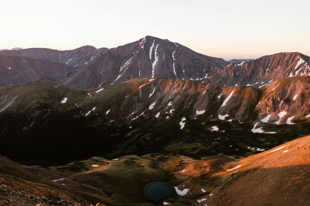 alpenglow on the snow lined mountains with a view of Torreys peak and a small lake from the summit of Mt Sniktau hike trail in Colorado