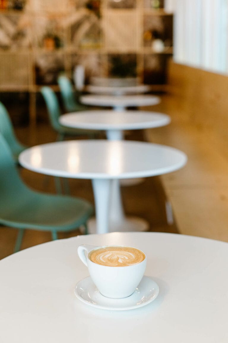 a latte in a white ceramic mug sitting on a round cafe table at a coffee shop