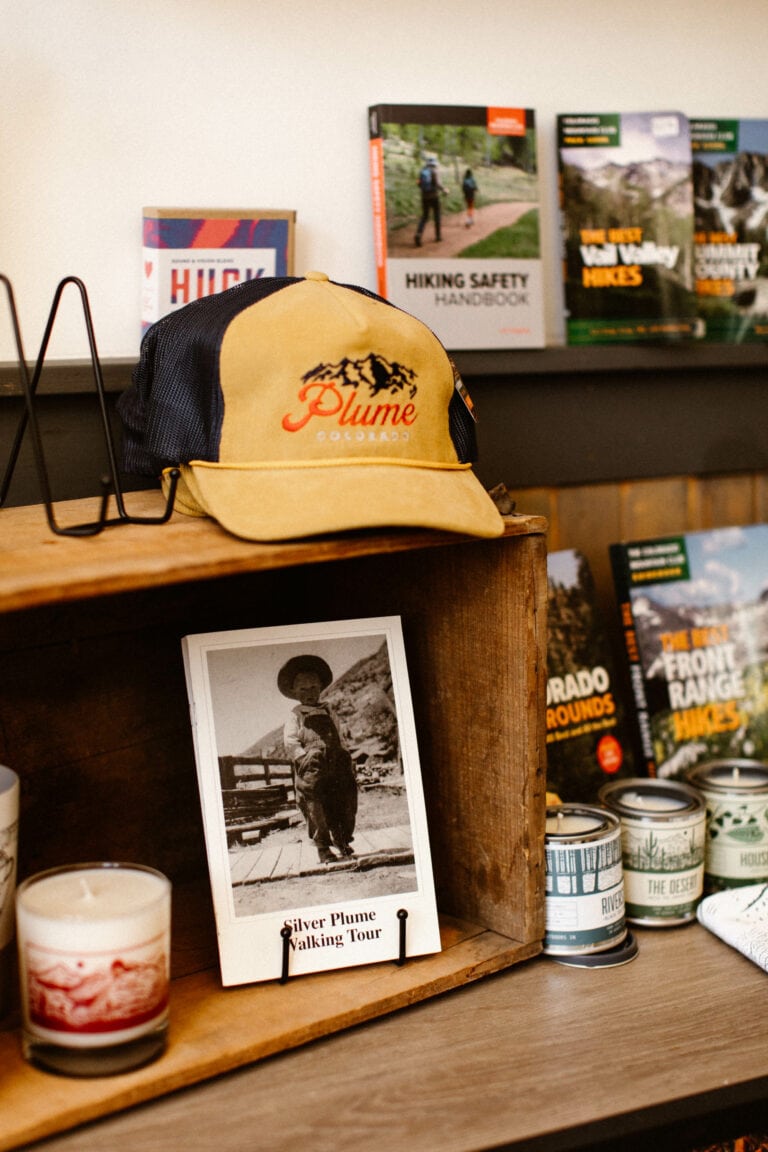 Colorado merchandise shelf at Plume Coffee Bar with a branded coffee shop hat and a Silver Plume themed black and white postcard